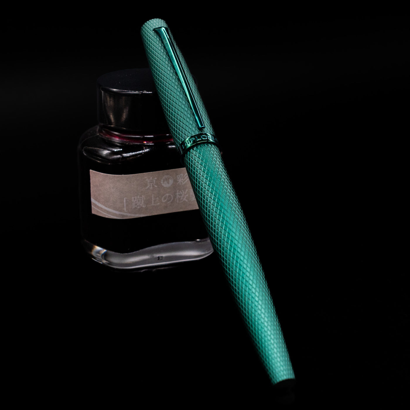 Diplomat Viper Rollerball Pen - Green capped, leaning against an ink bottle. 