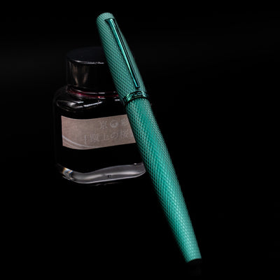Diplomat Viper Rollerball Pen - Green capped, leaning against an ink bottle. 