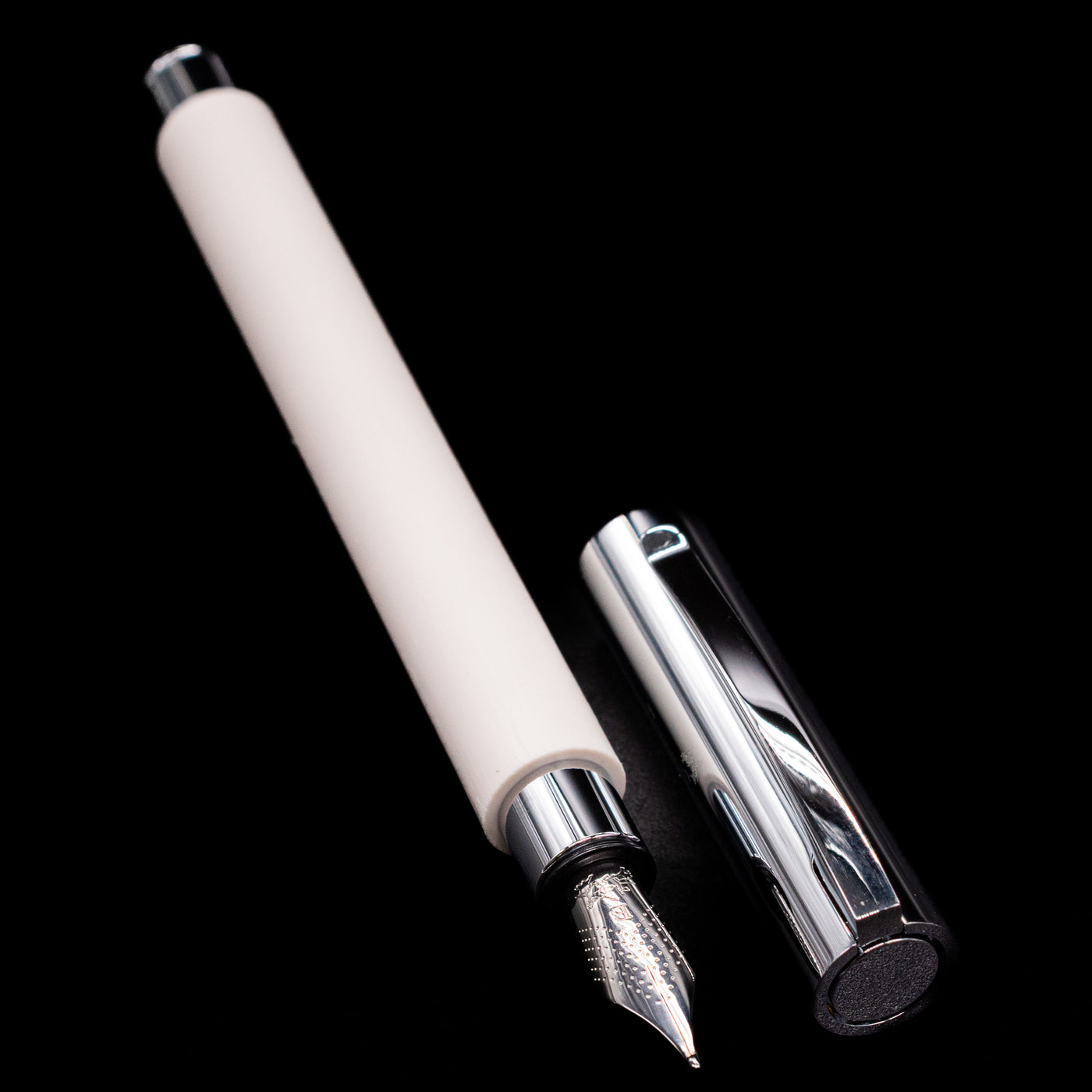A full view of the Faber-Castell Ambition Fountain Pen - Cinematic White uncapped, with its cap laying next to the pen. 