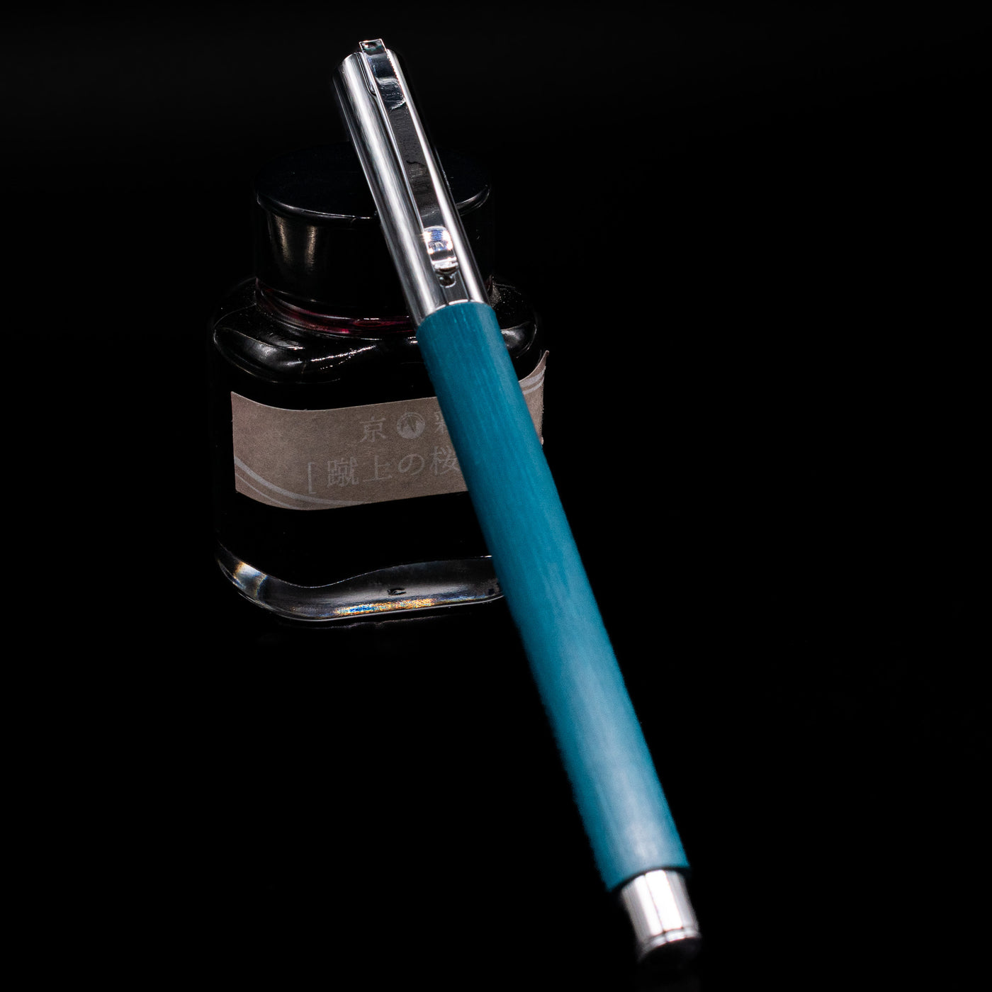 Faber-Castell Ambition Fountain Pen - Soft Teal (Limited Edition) capped, leaning against an ink bottle. 