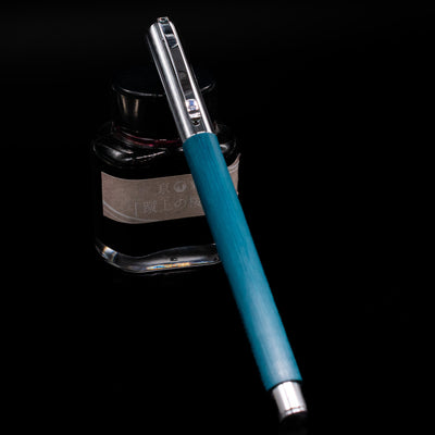 Faber-Castell Ambition Fountain Pen - Soft Teal (Limited Edition) capped, leaning against an ink bottle. 