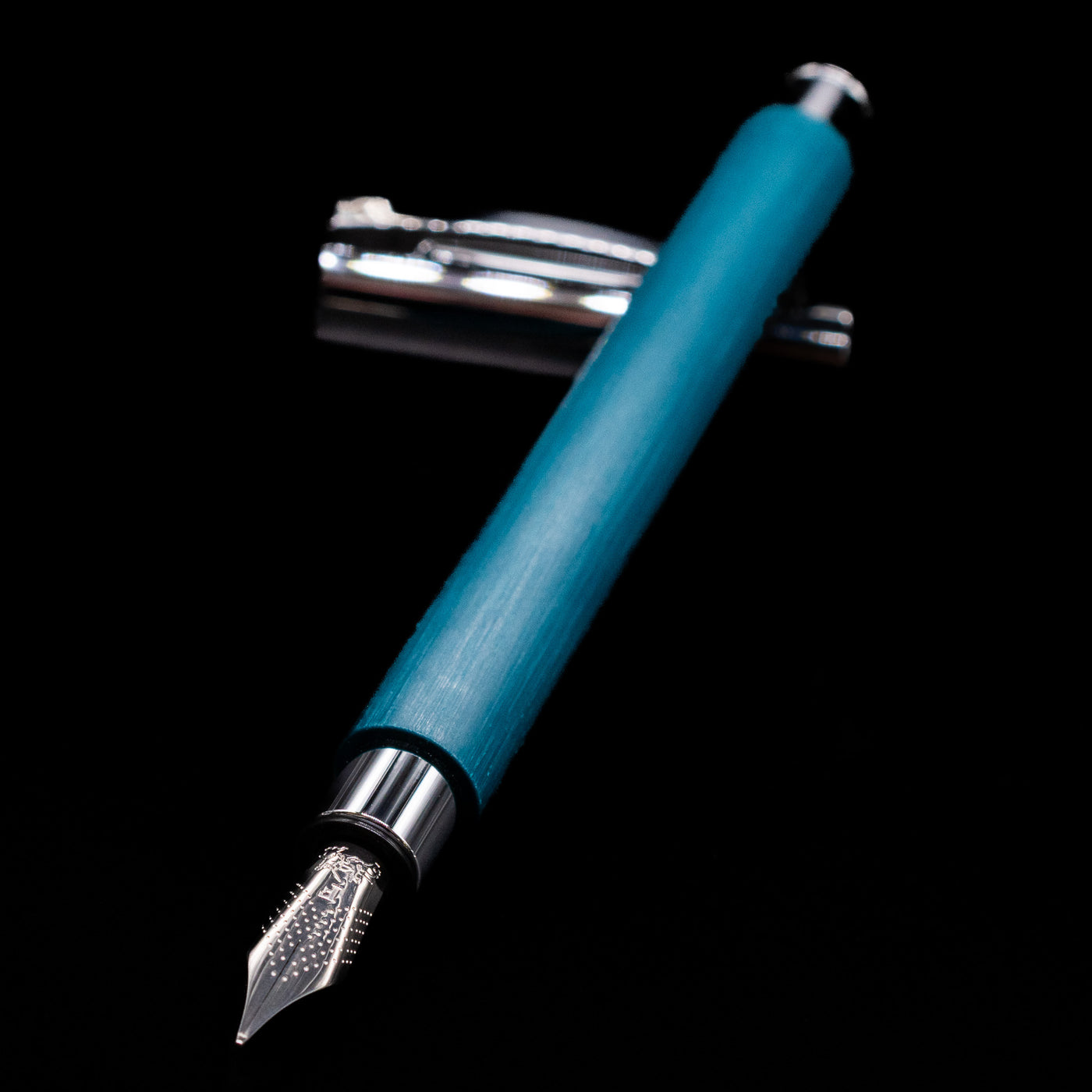 Faber-Castell Ambition Fountain Pen - Soft Teal (Limited Edition) laying across its own cap, crossed, with a focus on the nib.