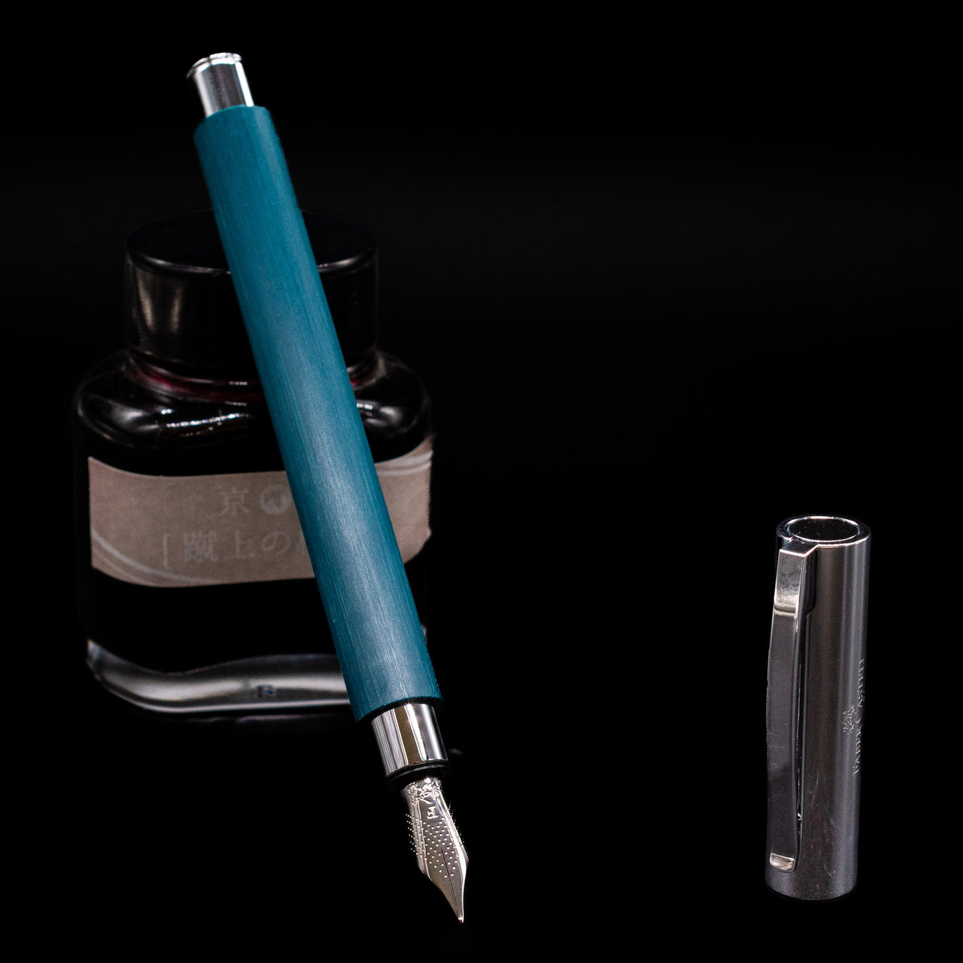 Faber-Castell Ambition Fountain Pen - Soft Teal (Limited Edition) leaning on an ink bottle uncapped showcasing the detailing on the nib.