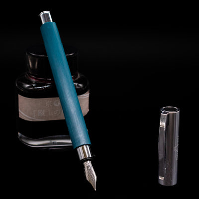 Faber-Castell Ambition Fountain Pen - Soft Teal (Limited Edition) leaning on an ink bottle uncapped showcasing the detailing on the nib.