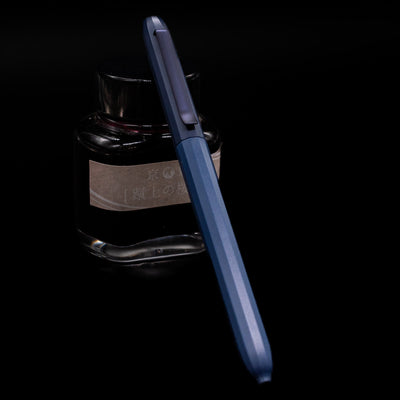 Faber-Castell Avori Ballpoint Pen - Midnight Muse leaning against an ink bottle.