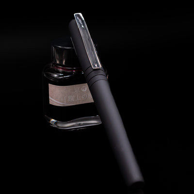 Faber-Castell Poly Fountain Pen - Black  capped, leaning against an ink bottle. 