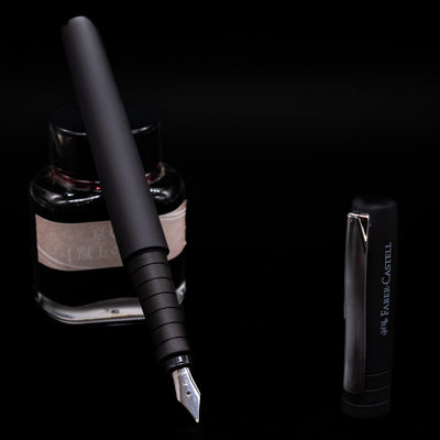 Faber-Castell Poly Fountain Pen - Black leaning on an ink bottle uncapped showcasing the detailing on the nib.