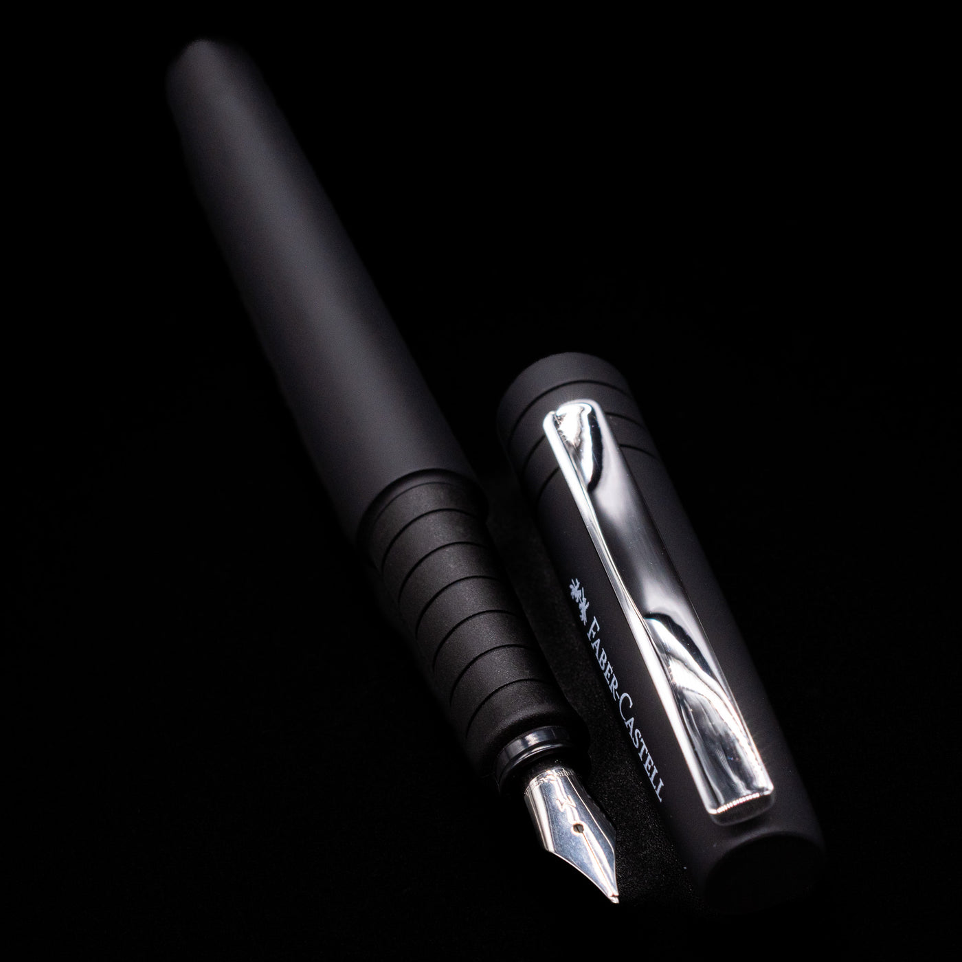 A full view of the Faber-Castell Poly Fountain Pen - Black uncapped, with its cap laying next to the pen. 