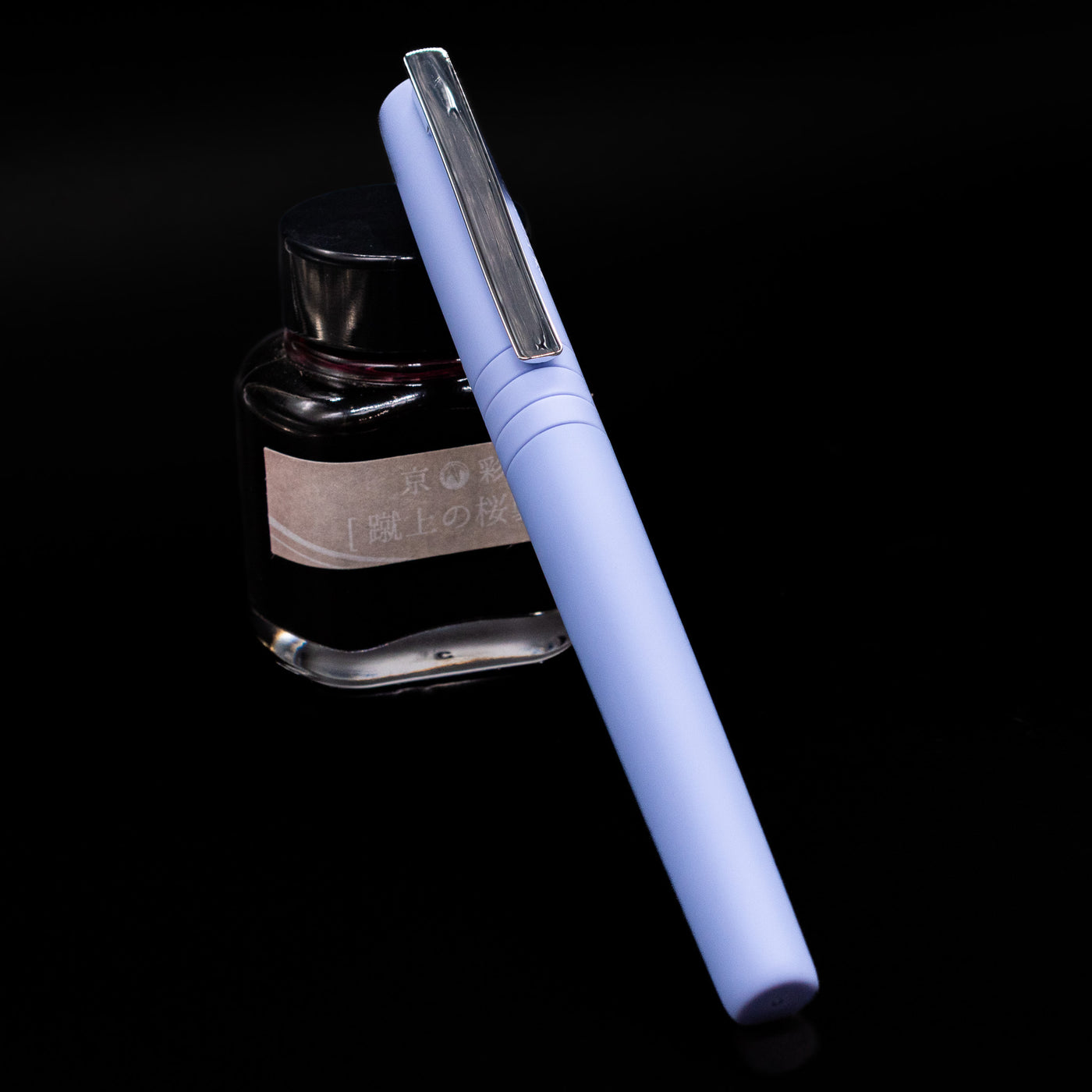 Faber-Castell Poly Fountain Pen - Caribic Blue capped, leaning against an ink bottle. 