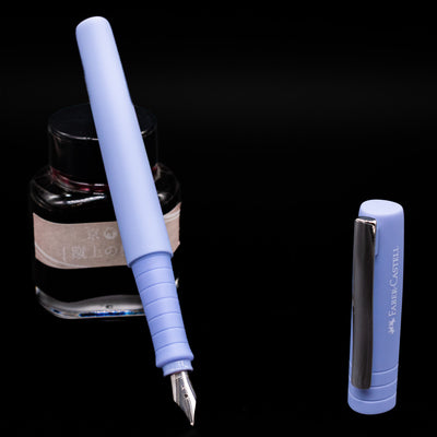 Faber-Castell Poly Fountain Pen - Caribic Blue leaning on an ink bottle uncapped showcasing the detailing on the nib.