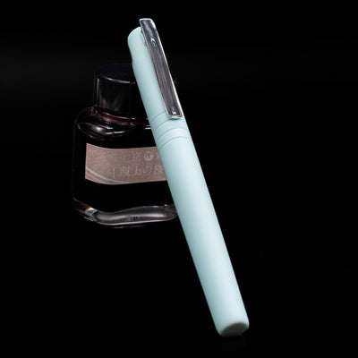 Faber-Castell Poly Fountain Pen - Iris capped, leaning against an ink bottle. 