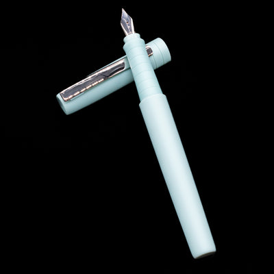 Faber-Castell Poly Fountain Pen - Iris  laying on top of its cap in a crossed position showing full view of the entire uncapped pen.