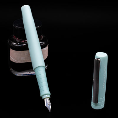 Faber-Castell Poly Fountain Pen - Iris  leaning on an ink bottle uncapped showcasing the detailing on the nib.
