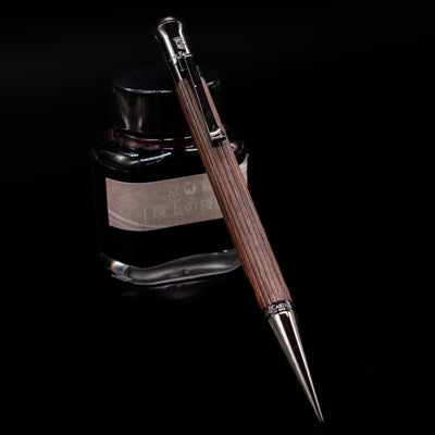 Graf von Faber-Castell Classic Mechanical Pencil - Macassar Wood leaning on an ink bottle.