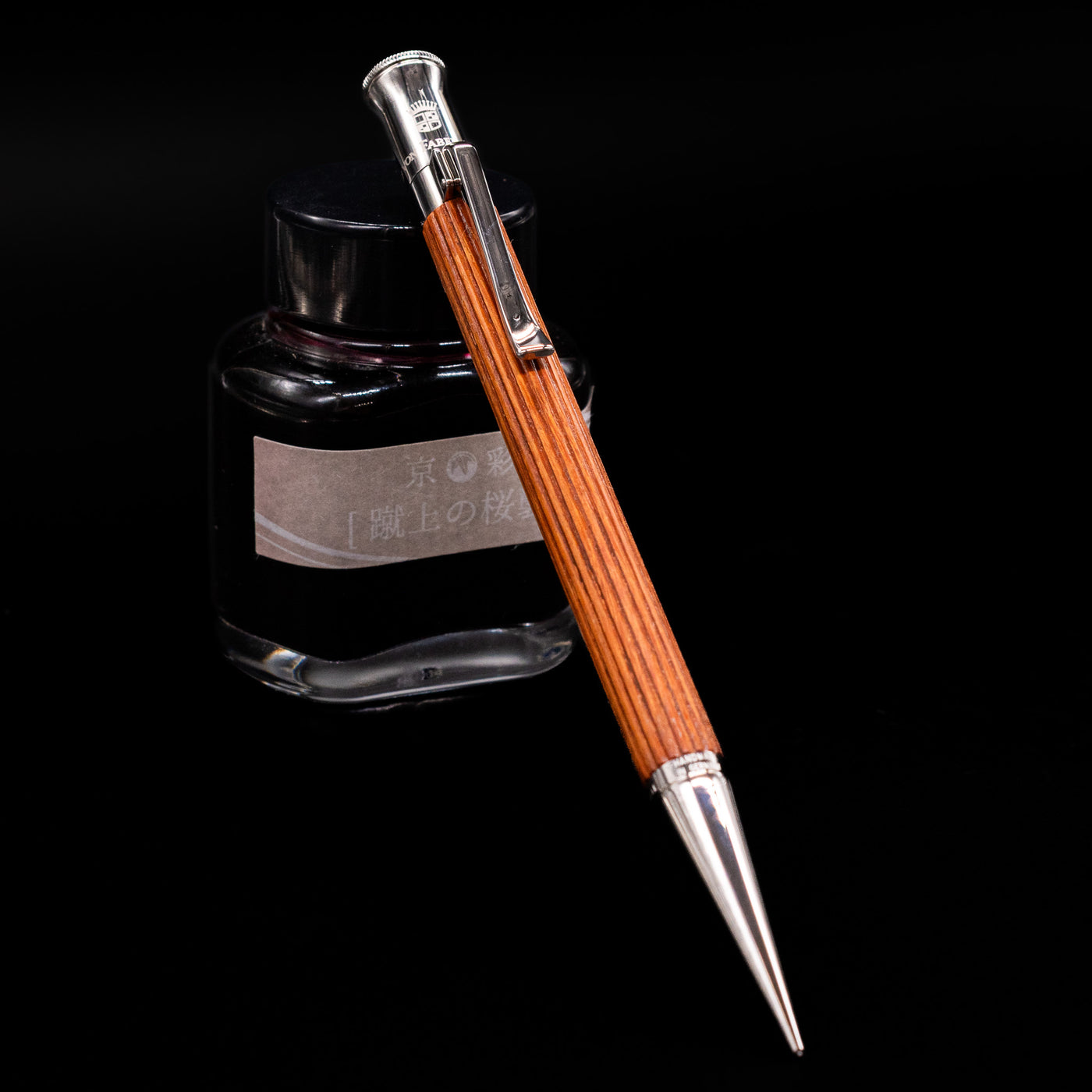 Graf von Faber-Castell Classic Mechanical Pencil - Pernambuco Wood leaning against an ink bottle.