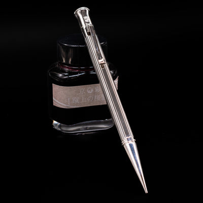 Graf von Faber-Castell Classic Mechanical Pencil - Platinum Plated leaning on an ink bottle.