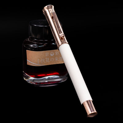Graf von Faber-Castell Guilloche Fountain Pen - Champagne Blush capped, leaning against an ink bottle. 