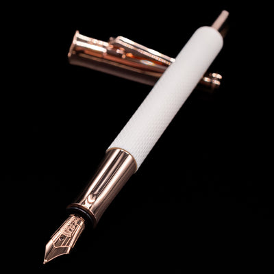 Graf von Faber-Castell Guilloche Fountain Pen - Champagne Blush laying across its own cap, crossed, with a focus on the nib.