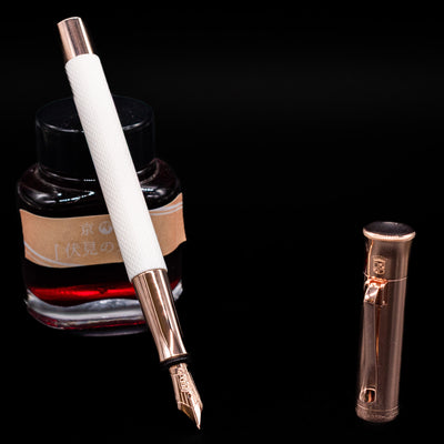 Graf von Faber-Castell Guilloche Fountain Pen - Champagne Blush leaning on an ink bottle uncapped showcasing the detailing on the nib.