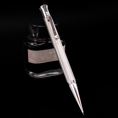 Graf von Faber-Castell Guilloche Mechanical Pencil - Barley Rhodium leaning against an ink bottle.