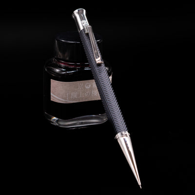 Graf von Faber-Castell Guilloche Mechanical Pencil - Cisele Anthracite leaning on an ink bottle.