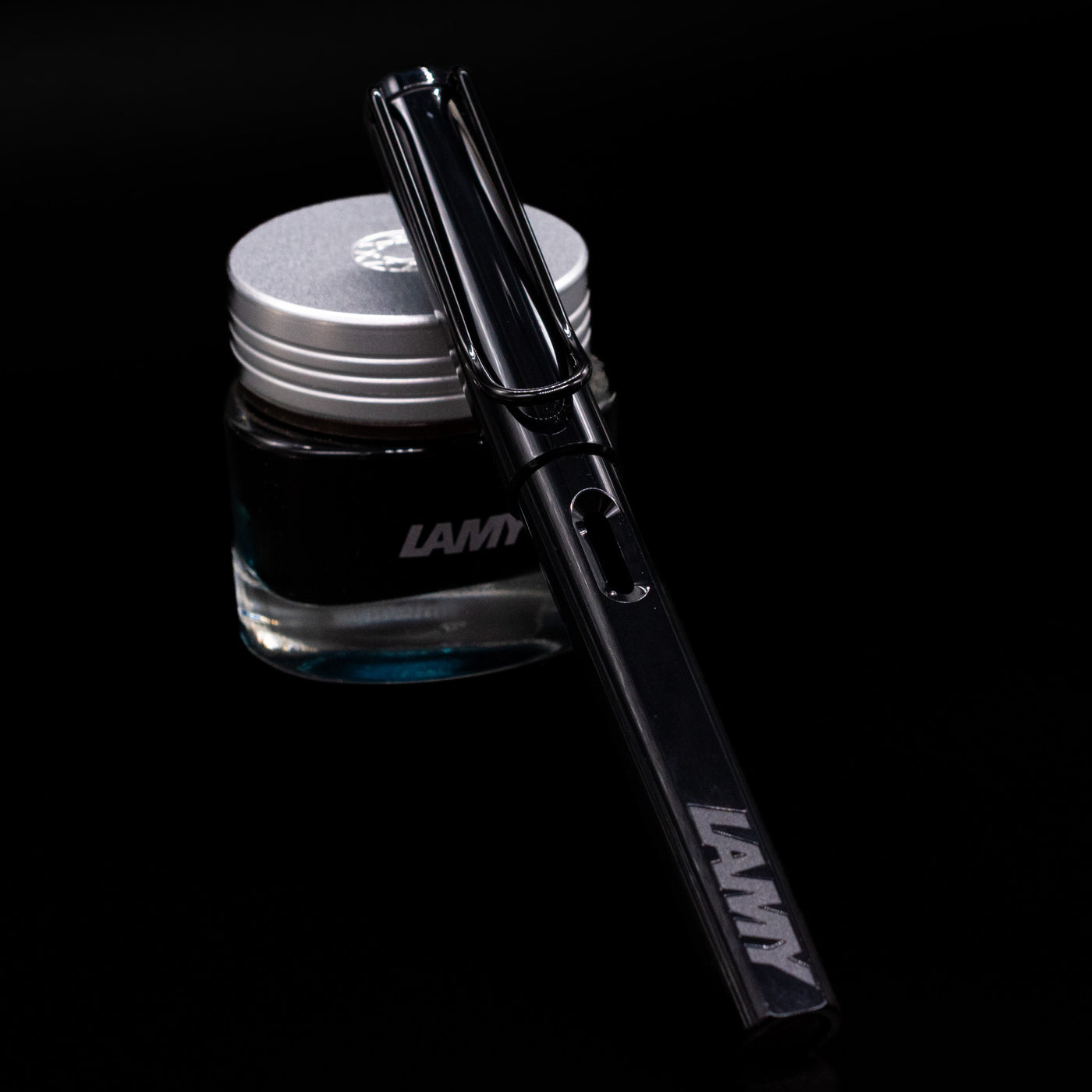 LAMY Safari Multi Fountain Pen in glossy black, capped, resting diagonally on an ink bottle.