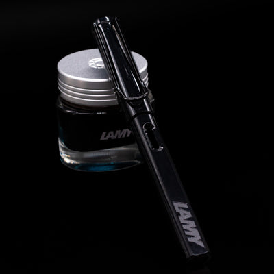 LAMY Safari Multi Fountain Pen in glossy black, capped, resting diagonally on an ink bottle.