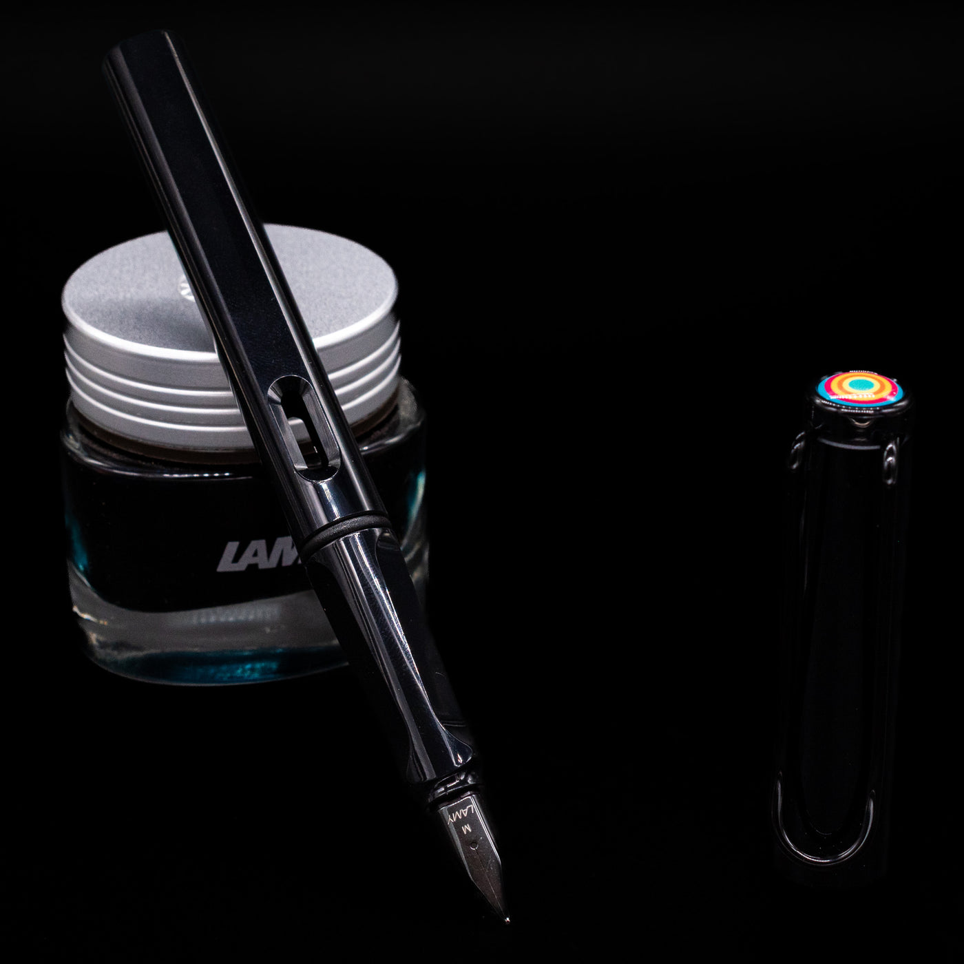 Glossy black LAMY Safari Multi pen with nib exposed, uncapped, leaning against an ink bottle.