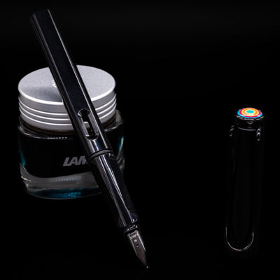 Glossy black LAMY Safari Multi pen with nib exposed, uncapped, leaning against an ink bottle.