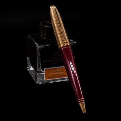 Louis Vuitton Doc Lacquer Burgundy & Gold Ballpoint Pen - Preowned leaning on an ink bottle.