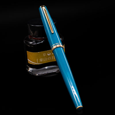 Montblanc Generation Turquoise Fountain Pen - Preowned capped, leaning against an ink bottle. 