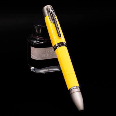 Montblanc Great Characters Enzo Ferrari Fountain Pen - Giallo Modena capped, leaning against an ink bottle. 