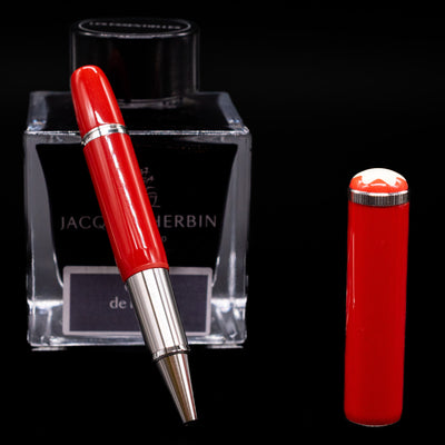 Montblanc Heritage Baby Rollerball Pen - Coral leaning on an ink bottle uncapped.