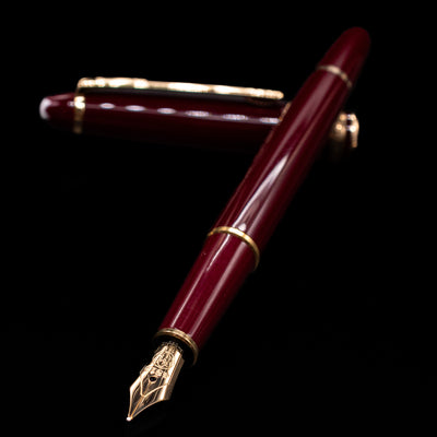 Montblanc Meisterstuck 144R Bordeaux Fountain Pen - Preowned laying across its own cap, crossed, with a focus on the nib.