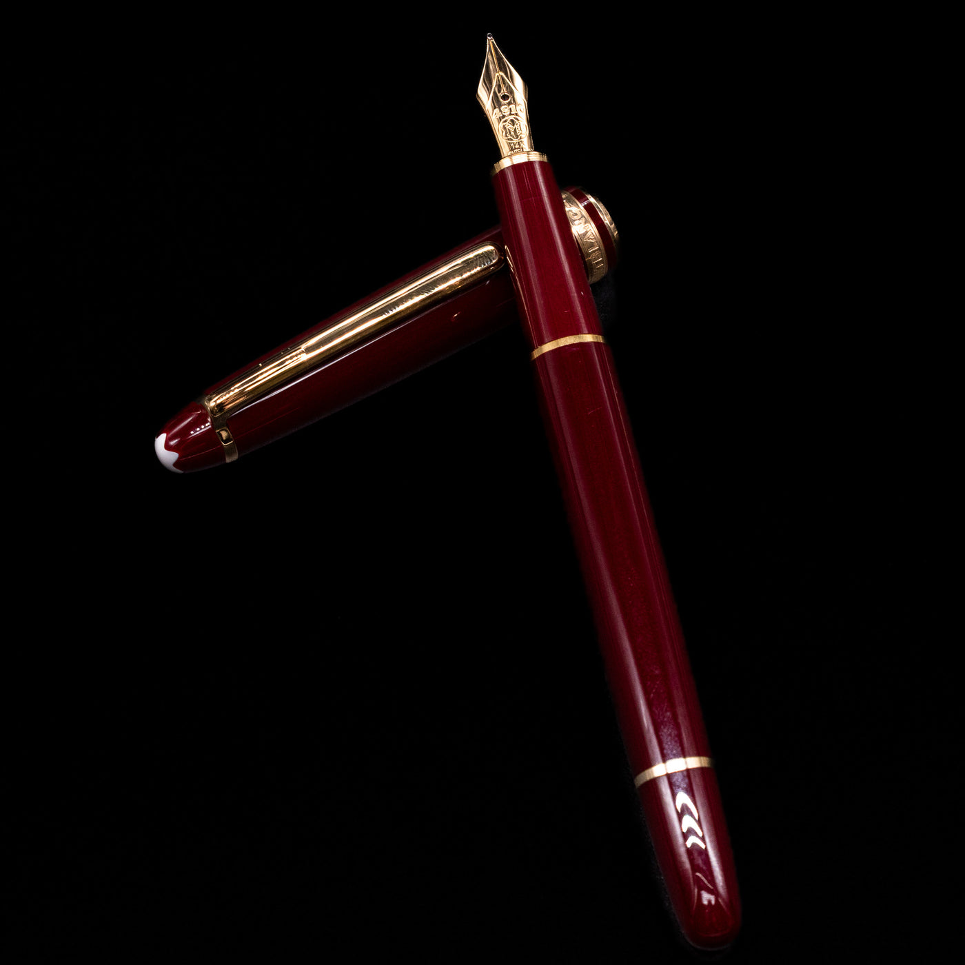 Montblanc Meisterstuck 144R Bordeaux Fountain Pen - Preowned laying on top of its cap in a crossed position showing full view of the entire uncapped pen.