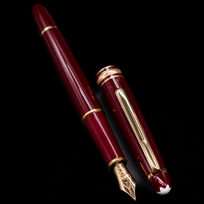 A full view of the Montblanc Meisterstuck 144R Bordeaux Fountain Pen - Preowned uncapped, with its cap laying next to the pen. 