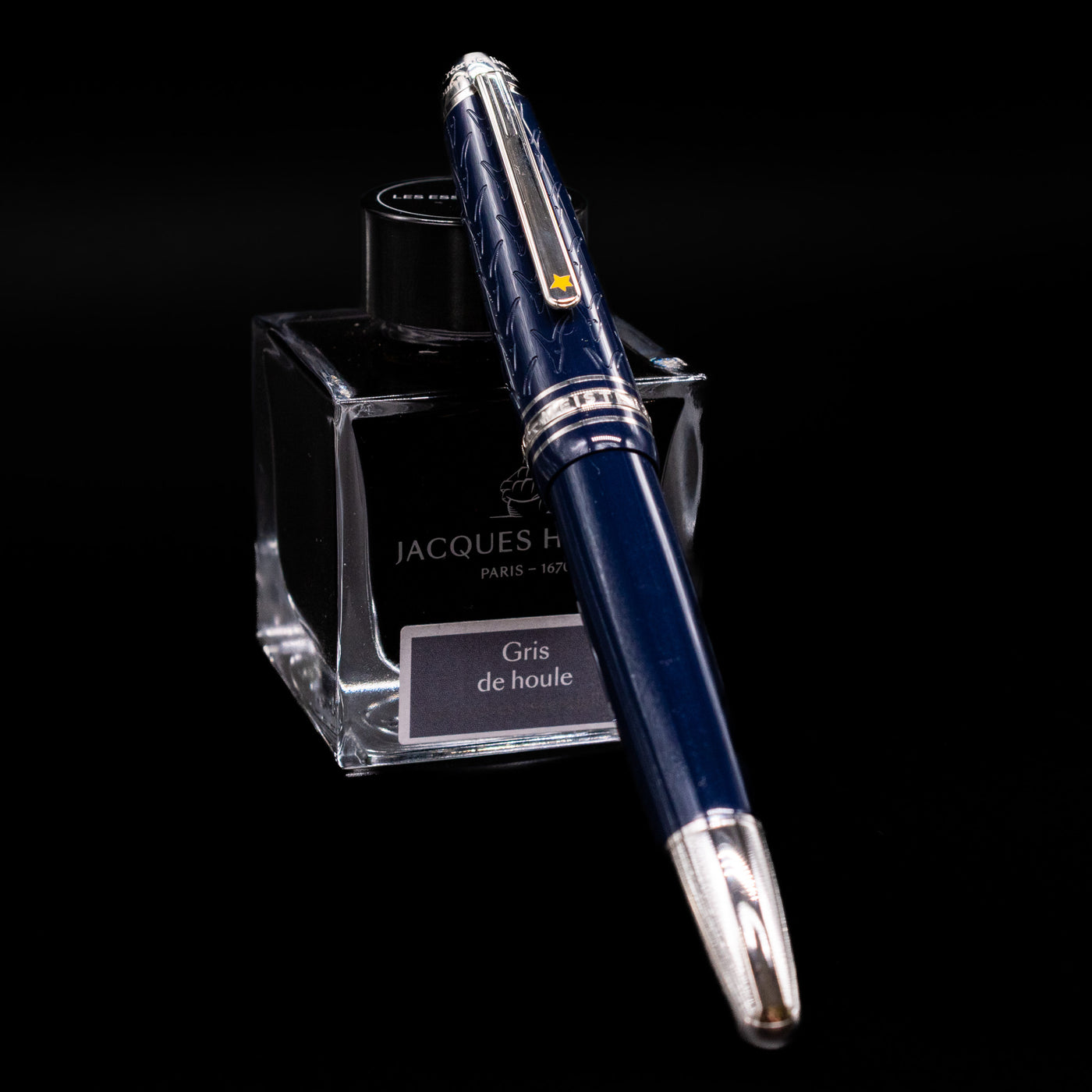 Preowned Montblanc Meisterstück Le Petit Prince Fox LeGrand fountain pen shown capped, resting at an angle against an ink bottle. The deep blue resin body is accented with platinum-plated trim, and the cap features a platinum fox emblem inspired by The Little Prince.