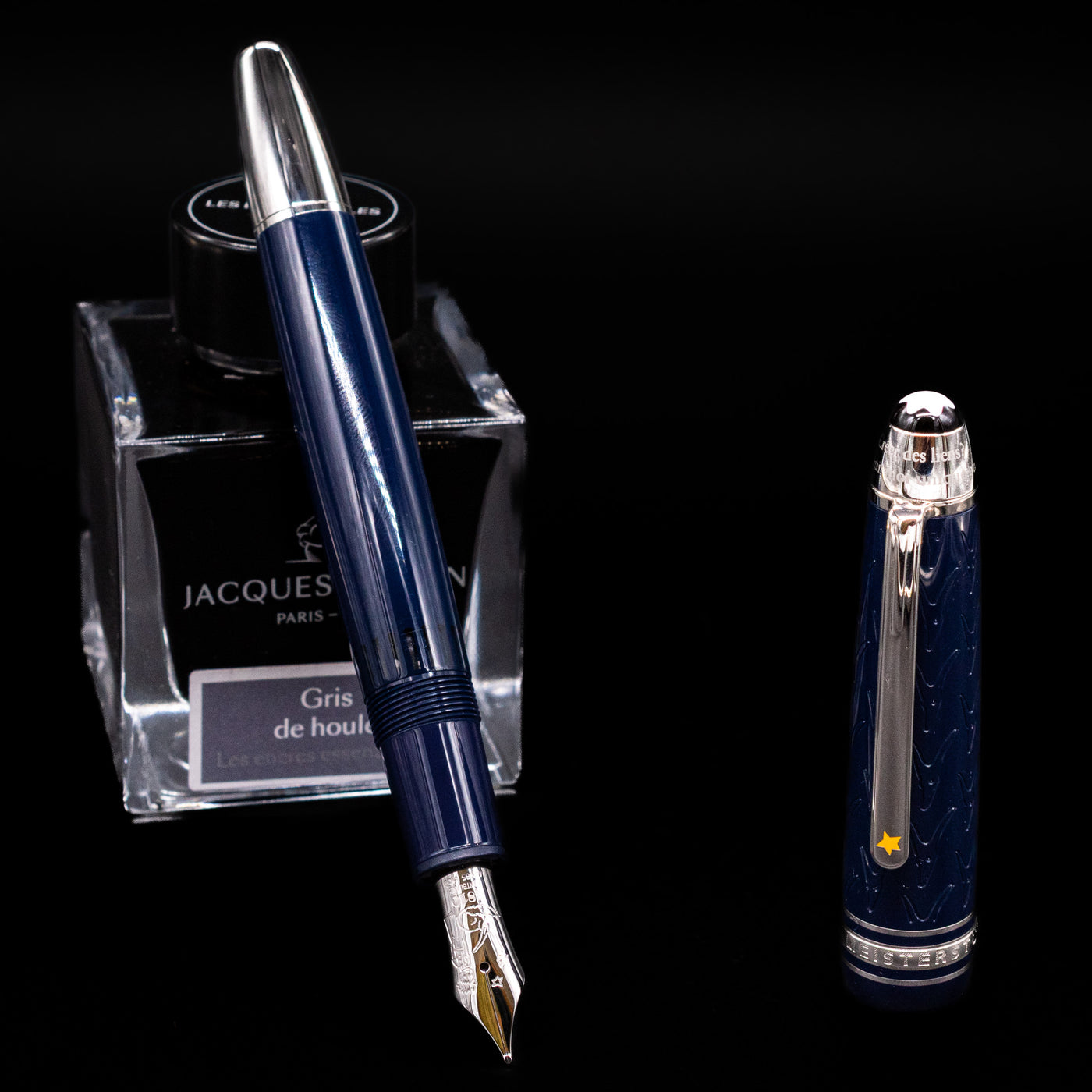 Preowned Montblanc Meisterstück Le Petit Prince Fox LeGrand fountain pen displayed uncapped, leaning on an ink bottle to reveal its rhodium-coated 14k gold nib engraved with the fox motif. The blue resin barrel and platinum accents give it a refined look.