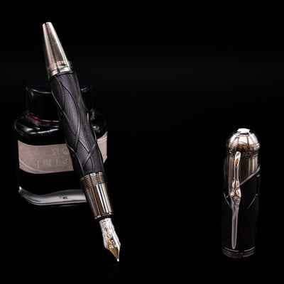 Montblanc Writer's Edition Brothers Grimm Fountain Pen leaning on an ink bottle uncapped showcasing the detailing on the nib.