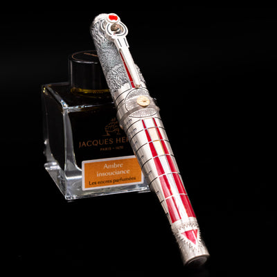 Montegrappa Alchemist Ignis Fountain Pen capped, leaning against an ink bottle. 