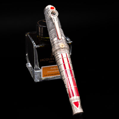 Montegrappa Alchemist Ignis Rollerbal Pen capped, leaning against an ink bottle. 