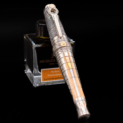 Montegrappa Alchemist Terra Rollerball Pen capped, leaning against an ink bottle. 