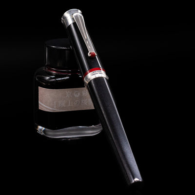 Montegrappa Desiderio Black Fountain Pen - Preowned capped, leaning against an ink bottle. 