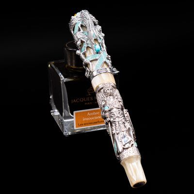 Montegrappa My Guardian Angel Rollerbal Pen capped, leaning against an ink bottle. 