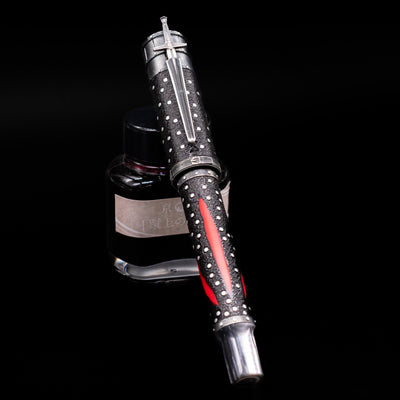 Montegrappa The Witcher: Mutation Fountain Pen capped, leaning against an ink bottle. 