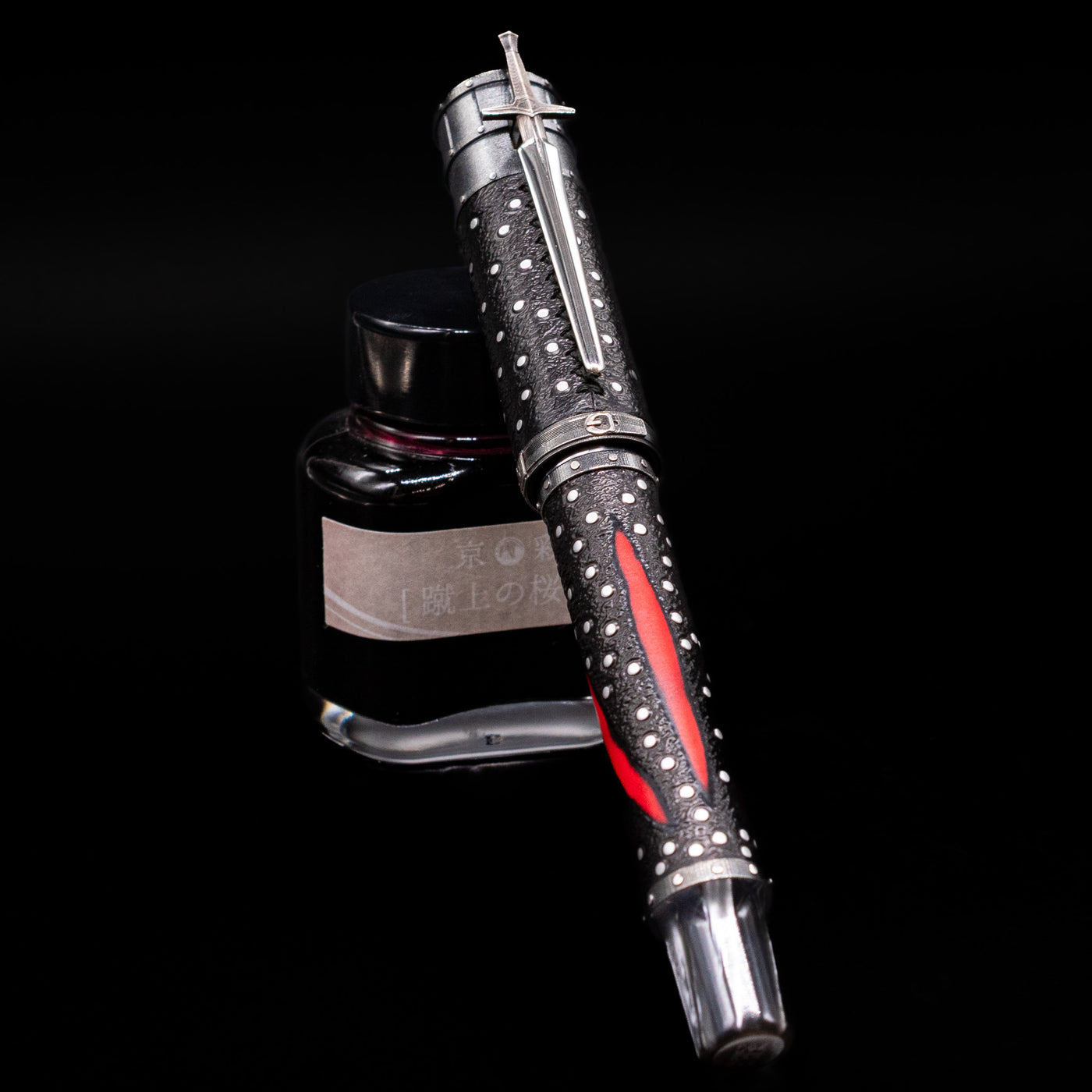 Montegrappa The Witcher: Mutation Rollerbal Pen capped, leaning against an ink bottle. 