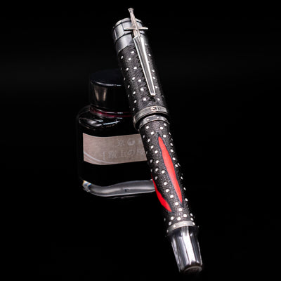 Montegrappa The Witcher: Mutation Rollerbal Pen capped, leaning against an ink bottle. 