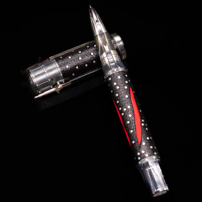 Montegrappa The Witcher: Mutation Rollerbal Pen laying on top of its cap in a crossed position showing full view of the entire uncapped pen.