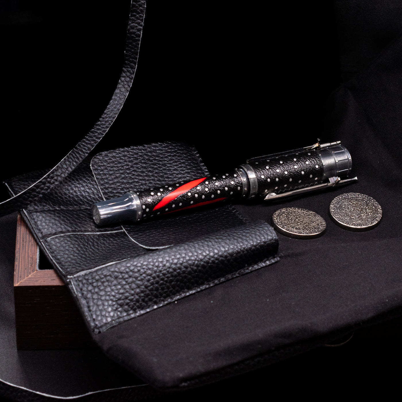 The leather pouch openned to see the Montegrappa The Witcher: Mutation Fountain Pen with 2 coins placed by its side.