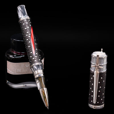 Montegrappa The Witcher: Mutation Rollerbal Pen leaning on an ink bottle uncapped.